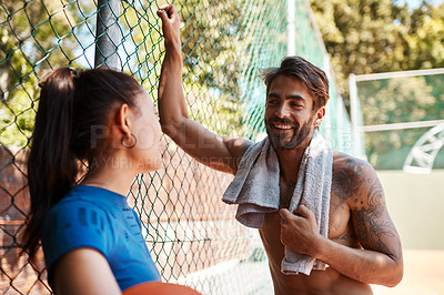 Buy stock photo Shot of two sporty young people chatting to each other against a fence on a sports court