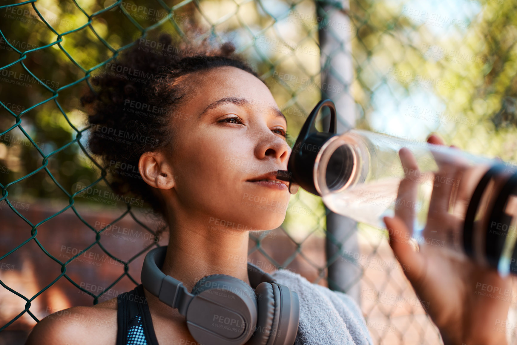 Buy stock photo Fitness, woman and drinking water outdoor for health, diet and wellness on break by fence. Sports, bottle and thirsty African athlete with liquid for hydration after exercise, workout and recovery