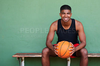 Buy stock photo Portrait of a sporty young man holding a basketball while sitting on a bench against a wall