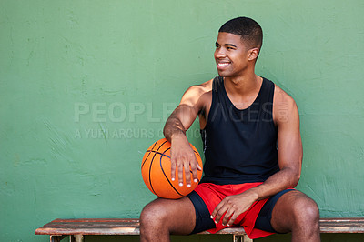 Buy stock photo Shot of a sporty young man holding a basketball while sitting on a bench against a wall