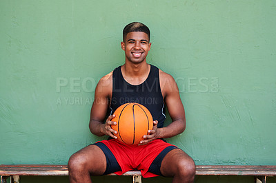 Buy stock photo Portrait of a sporty young man holding a basketball while sitting on a bench against a wall
