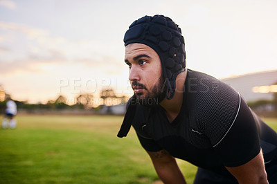 Buy stock photo Cropped shot of a handsome young sportsman wearing headgear and crouching alone during rugby practice during the day