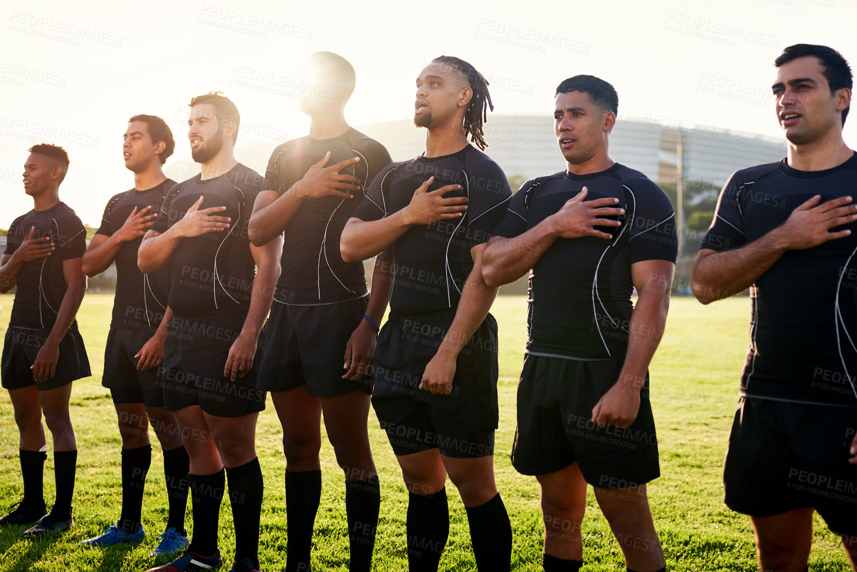 Buy stock photo Cropped shot of a diverse group of sportsmen standing together and singing their national anthem before playing rugby