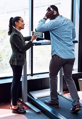 Buy stock photo Shot of a businessman walking on a treadmill while looking at something on a digital tablet with a colleague in an office