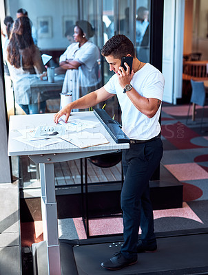 Buy stock photo Shot of a young businessman talking on a cellphone and going through paperwork while walking on a treadmill in an office