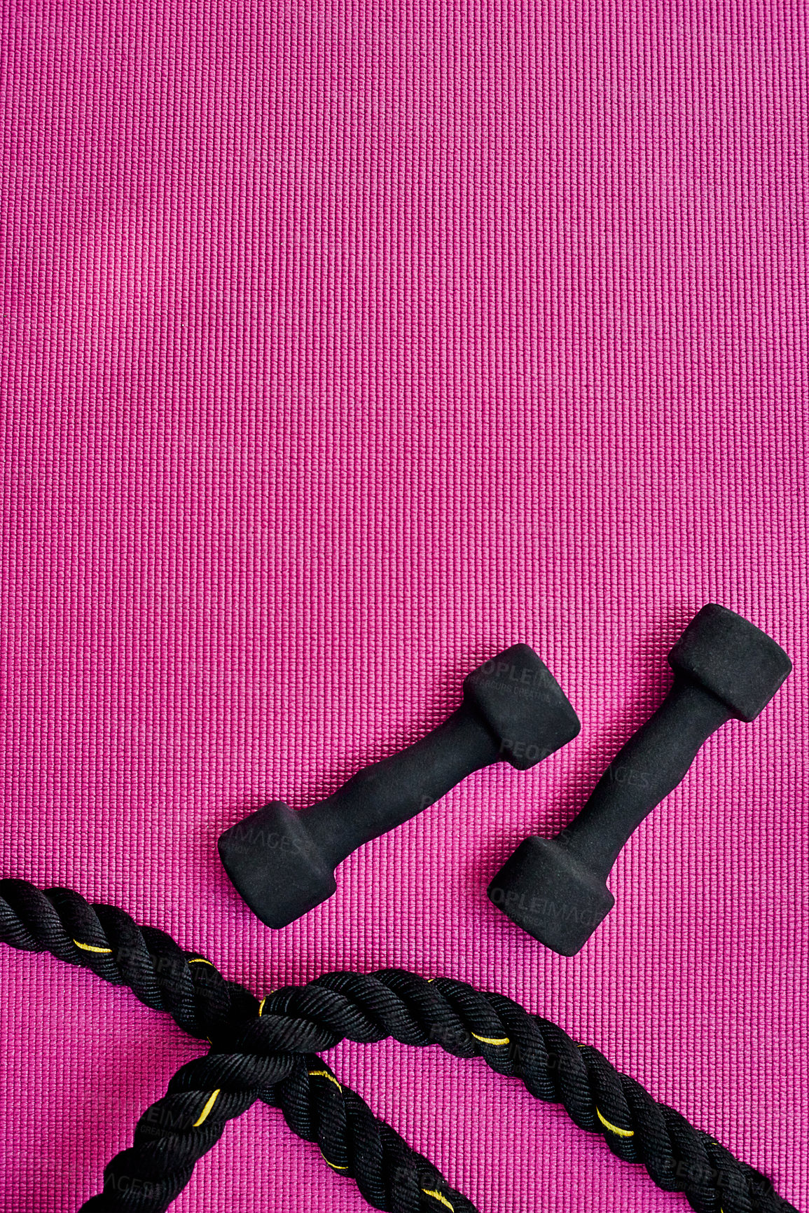 Buy stock photo High angle shot of two lightweight dumbbells and piece of rope placed on a pink background inside of a studio