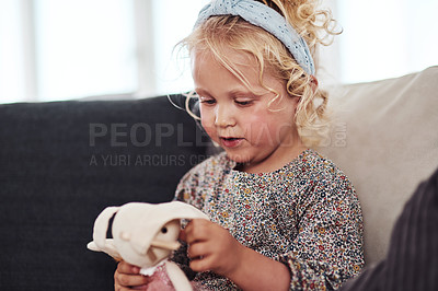 Buy stock photo Cropped shot of an adorable little girl sitting alone on the sofa and playing with her toys at home