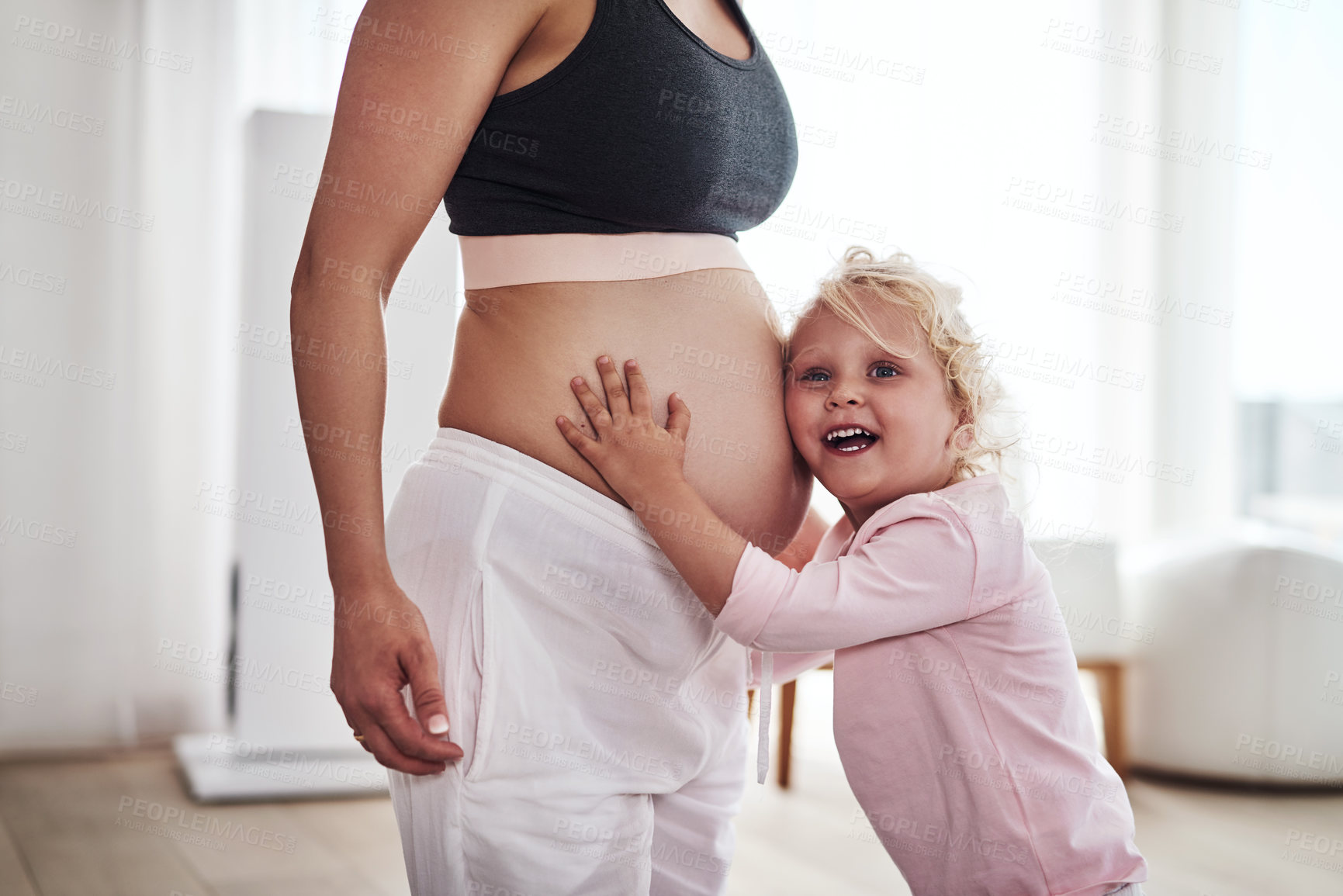 Buy stock photo Cropped shot of an adorable little girl standing and hugging her pregnant mother's tummy in the living room