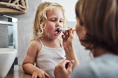 Buy stock photo Cropped shot of an adorable little girl standing and getting help from her mother while brushing her teeth