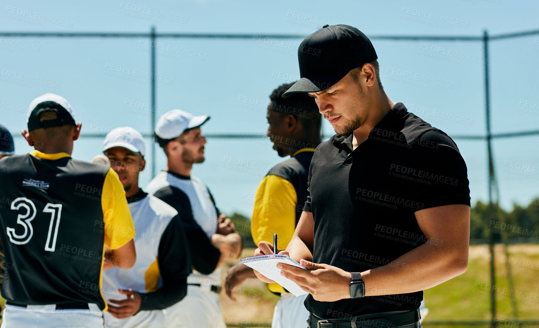 Buy stock photo Cropped shot of a handsome young baseball coach writing on a note pad while standing on the field during the day