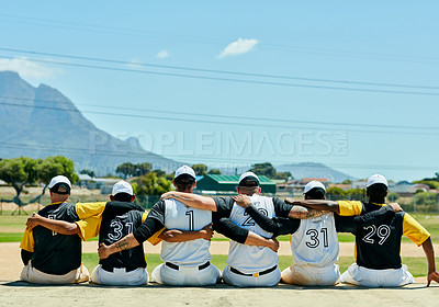 Buy stock photo Rearview shot of a team of unrecognizable baseball players embracing each other while sitting near a baseball field during the day