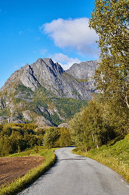 Buy stock photo A curvy road near a mountain and green plants outdoors with a cloudy blue sky background. Beautiful landscape of a tarred roadway surrounded by nature or forest on a summer afternoon