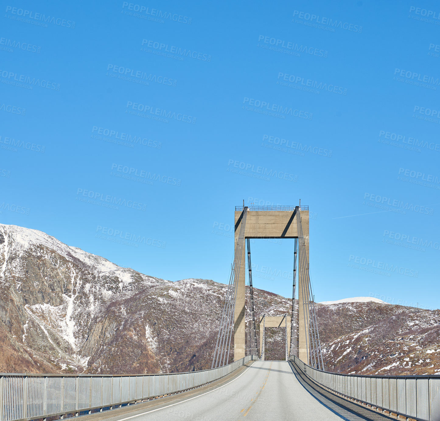Buy stock photo Empty road in the mountains against a blue sky with copy space. Deserted highway crossing in the cold snowy and grey hills around Bodo in Norway. Polar landscape of old bridge over a ravine or river