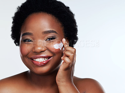Buy stock photo Studio shot of a beautiful young woman applying moisturiser to her face against a gray background