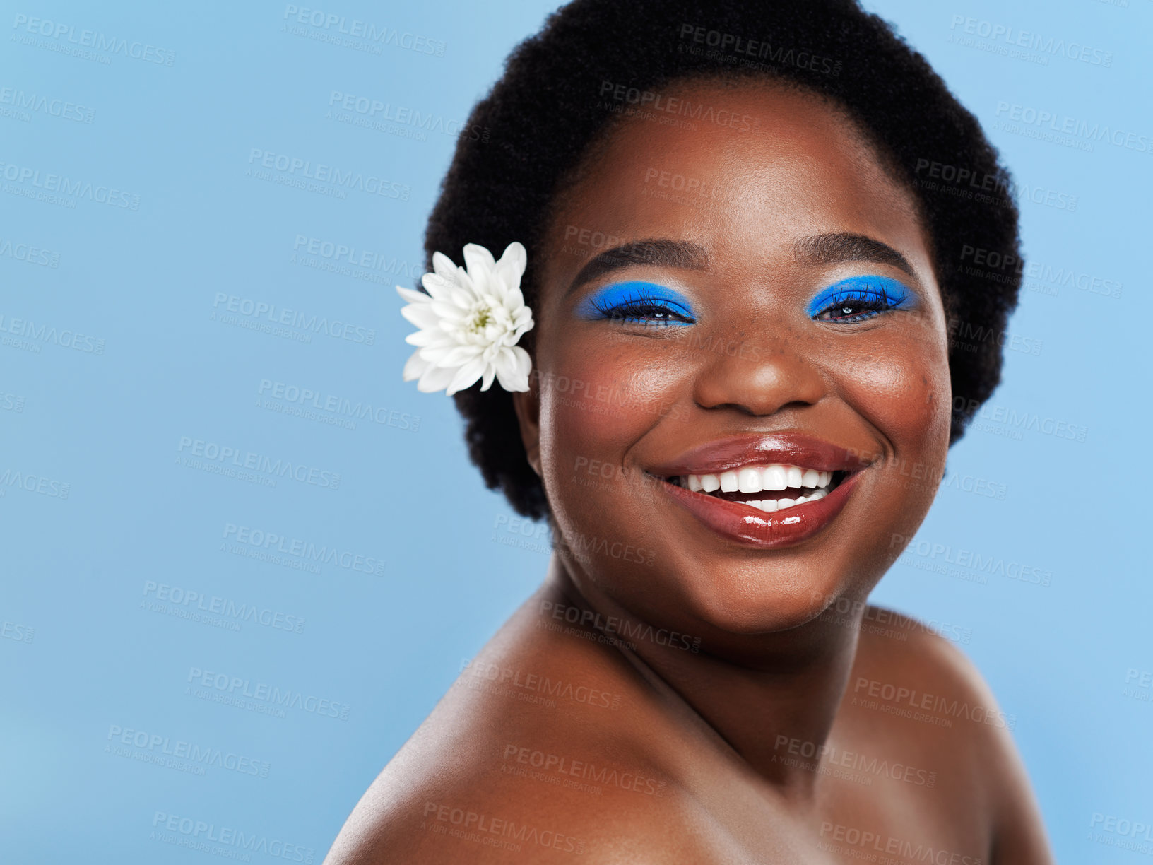 Buy stock photo Studio shot of a beautiful young woman with a flower behind her ear against a blue background