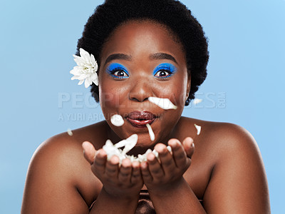 Buy stock photo Studio shot of a beautiful young woman blowing petals against a blue background