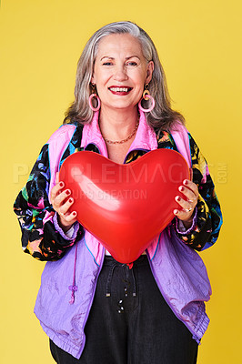 Buy stock photo Portrait of a confident and stylish senior woman holding a heart shaped balloon against a yellow background