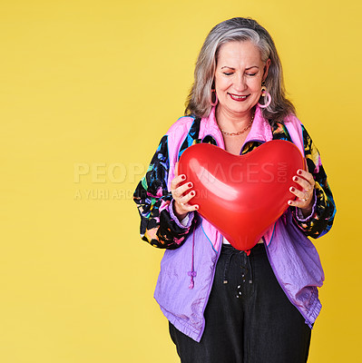 Buy stock photo Cropped shot of a confident and stylish senior woman holding a heart shaped balloon against a yellow background