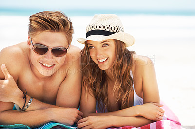 Buy stock photo Cropped shot of an affectionate young couple smiling while lying down together at the beach during the day