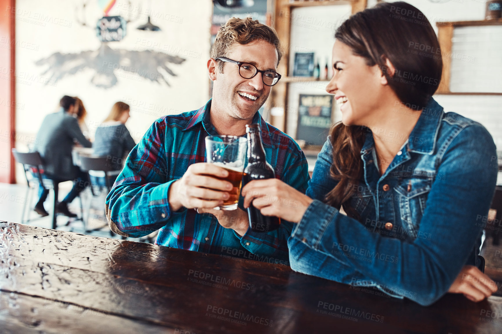 Buy stock photo Couple, cheers and beer in pub, fun and laughing with alcohol, together and blind date of woman with man. Bar, drinks and toast for people, love and relationship in weekend, bottle and romance