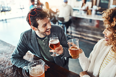 Buy stock photo Shot of a happy young man and woman toasting with beers at a bar