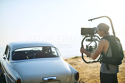 Buy stock photo Shot of a focused young man shooting a scene with people in a car with a state of the art video camera outside during the day