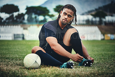 Buy stock photo Full length shot of a handsome young rugby player tying his shoelaces while sitting in the playing field during the day