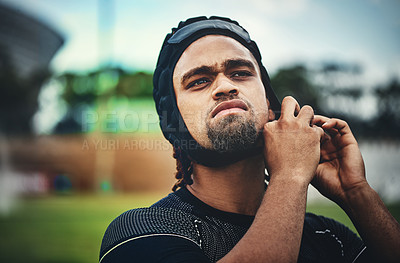 Buy stock photo Cropped shot of a handsome young rugby player adjusting his headgear while standing on the field during the day