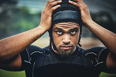 Buy stock photo Cropped shot of a handsome young rugby player adjusting his headgear while standing on the field during the day