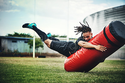 Buy stock photo Full length shot of a handsome young rugby player working out with a tackle bag on the playing field