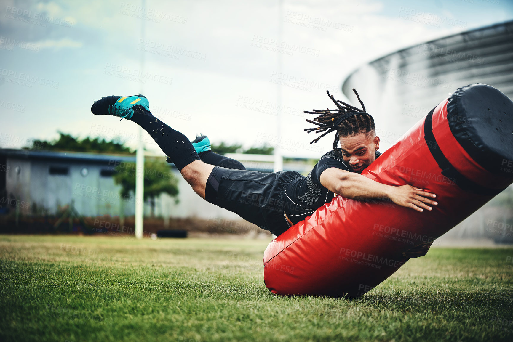 Buy stock photo Full length shot of a handsome young rugby player working out with a tackle bag on the playing field