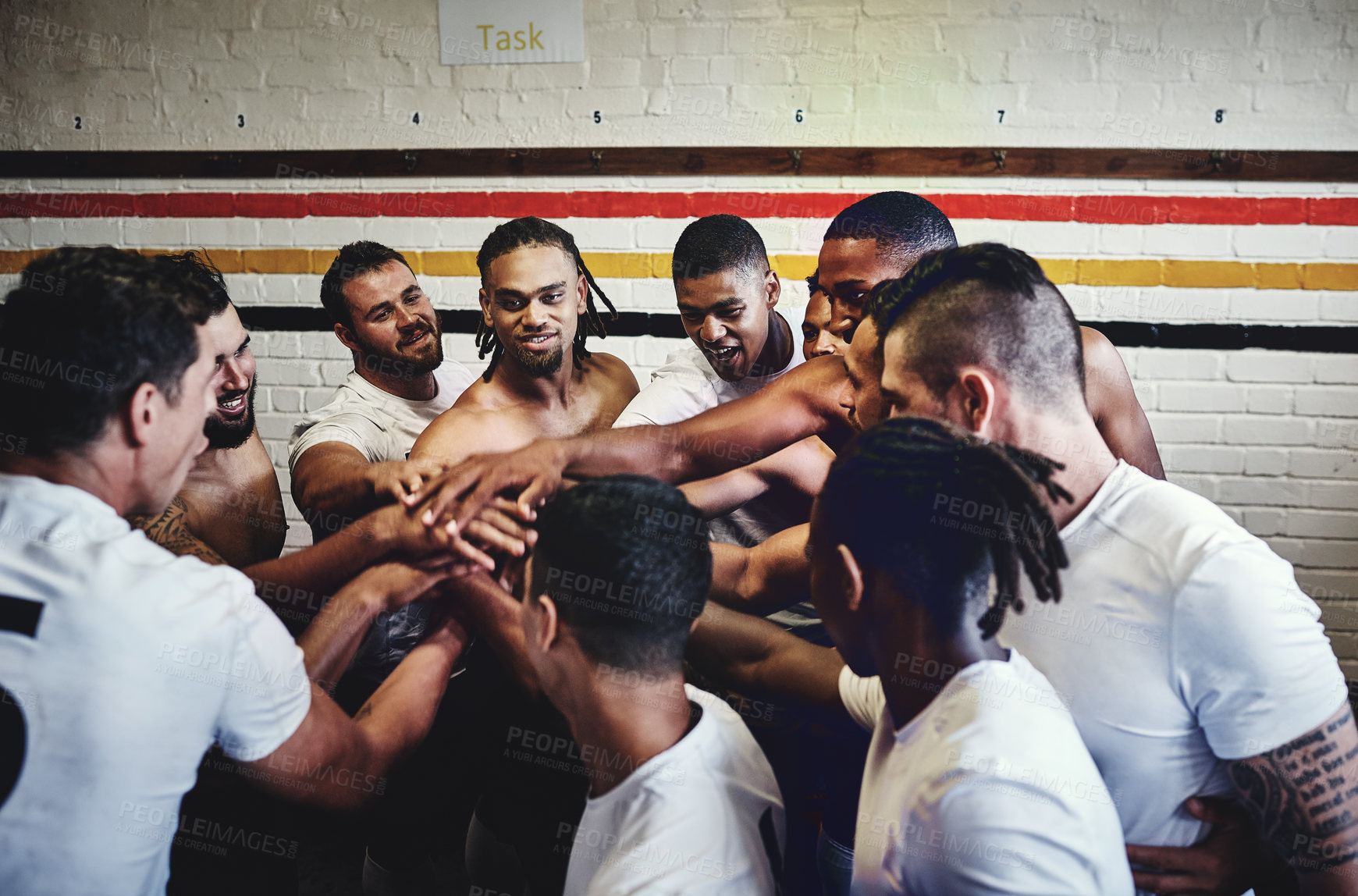 Buy stock photo Cropped shot of a group of handsome young rugby players standing together in a huddle in a locker room