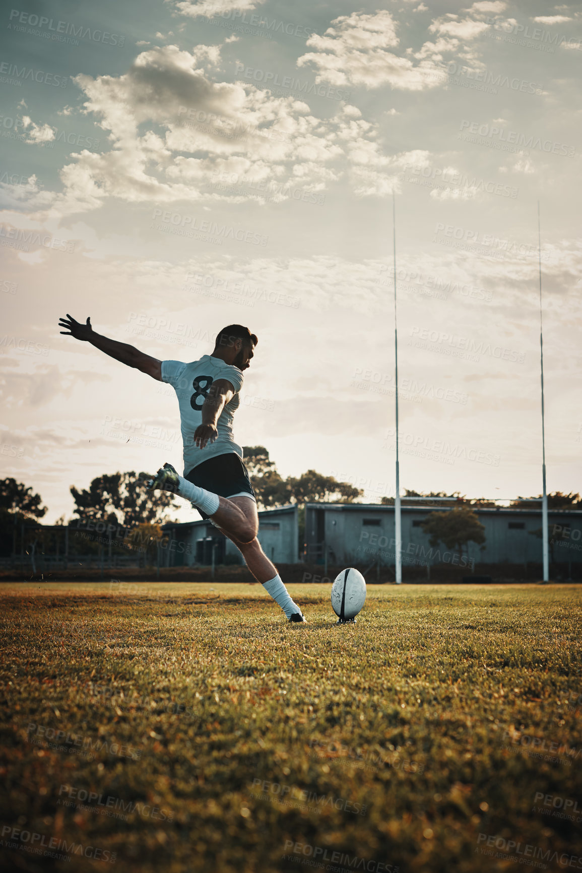 Buy stock photo Full length shot of a handsome young rugby player kicking a ball on the field during the day