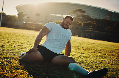 Buy stock photo Cropped shot of a handsome young rugby player stretching while training on the field during the day