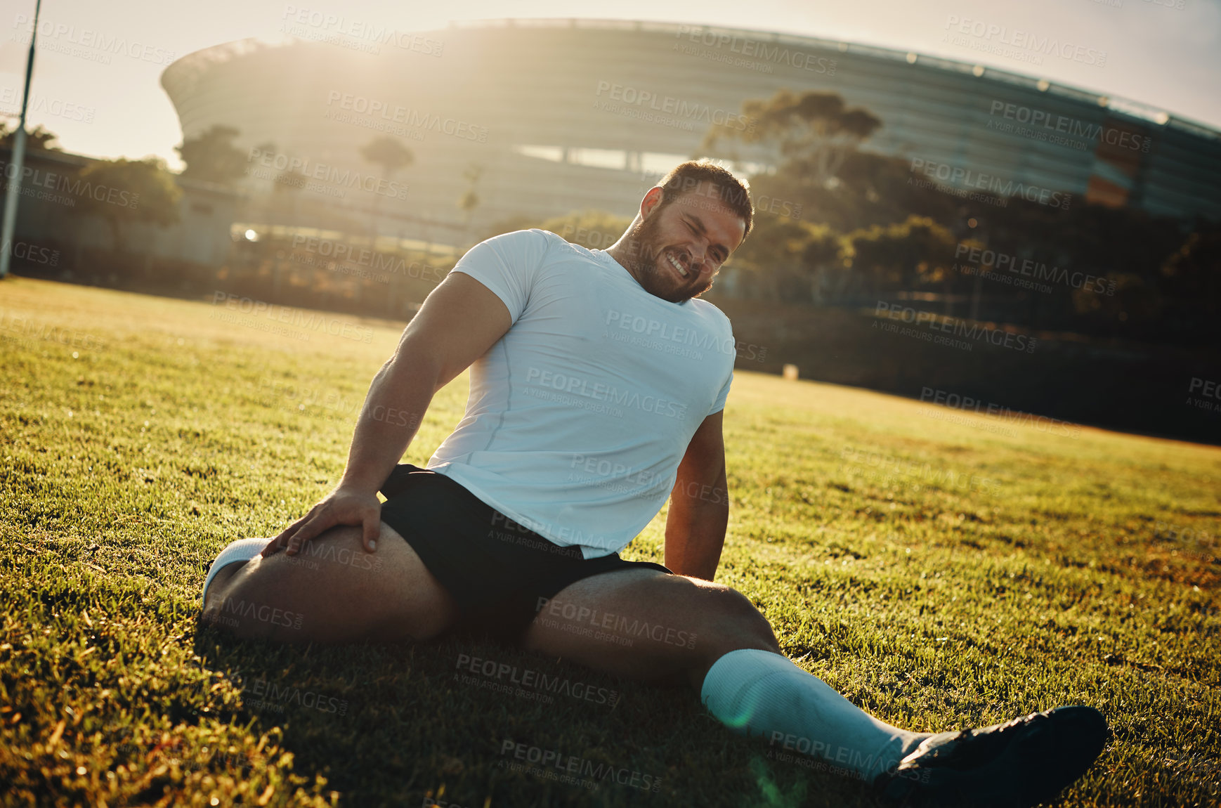 Buy stock photo Cropped shot of a handsome young rugby player stretching while training on the field during the day