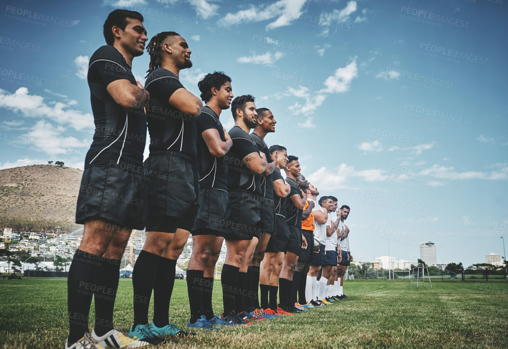 Buy stock photo Shot of a team of confident young rugby players standing at attention singing their anthem outside on a field before a rugby match