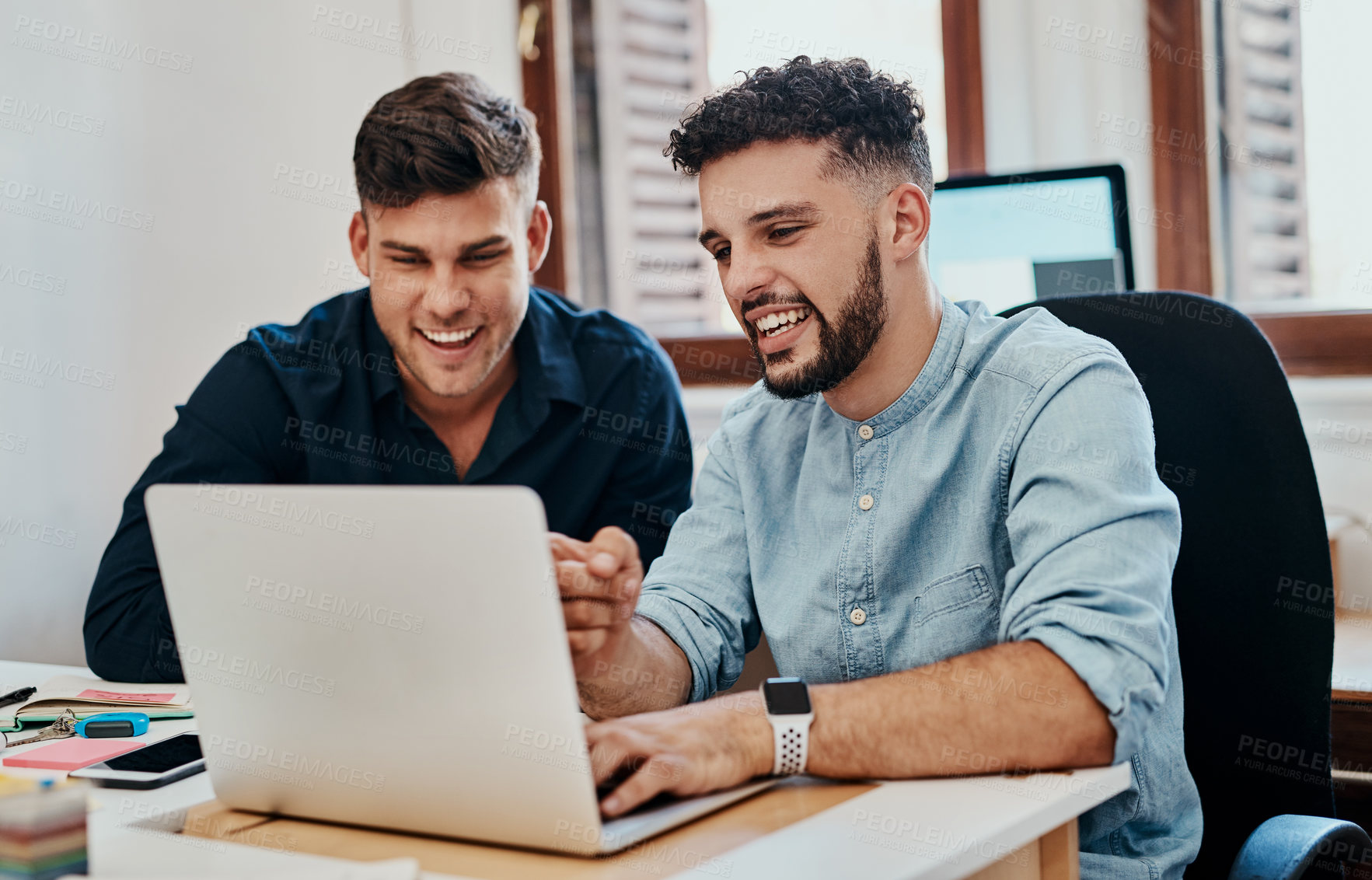 Buy stock photo Shot of two young businessmen using a laptop together in a modern office
