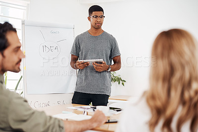 Buy stock photo Shot of a young businessman using a digital tablet while giving a presentation in an office