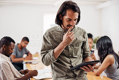 Buy stock photo Shot of a young businessman using a digital tablet in an office with his colleagues in the background