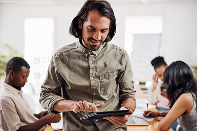 Buy stock photo Shot of a young businessman using a digital tablet in an office with his colleagues in the background