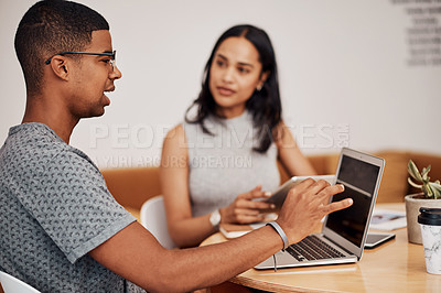 Buy stock photo Shot of a young businessman using a laptop while having a discussion with a colleague in an office