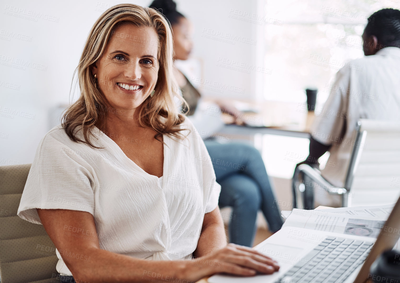 Buy stock photo Cropped portrait of an attractive young businesswoman sitting in her office with her coworkers and using her laptop
