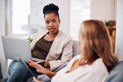 Buy stock photo Cropped shot of two attractive young businesswomen sitting in the office together and using technology during a discussion