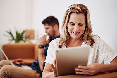Buy stock photo Cropped shot of an attractive young businesswoman sitting and using a tablet while her colleagues work behind her