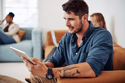Buy stock photo Cropped shot of a handsome young businessman sitting and using a tablet while his colleague works beside him