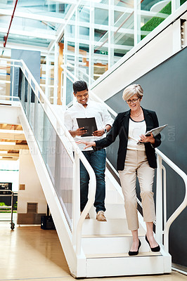 Buy stock photo Shot of two businesspeople walking down a staircase together in an office