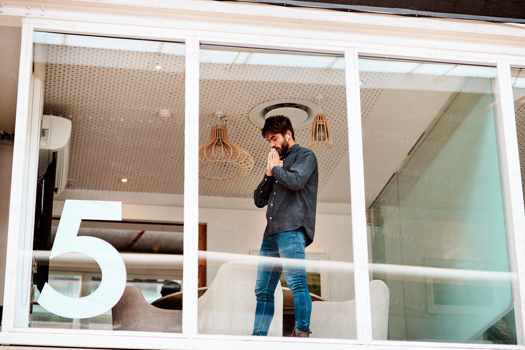 Buy stock photo Shot of a young businessman looking anxious while standing at a glass wall in an office