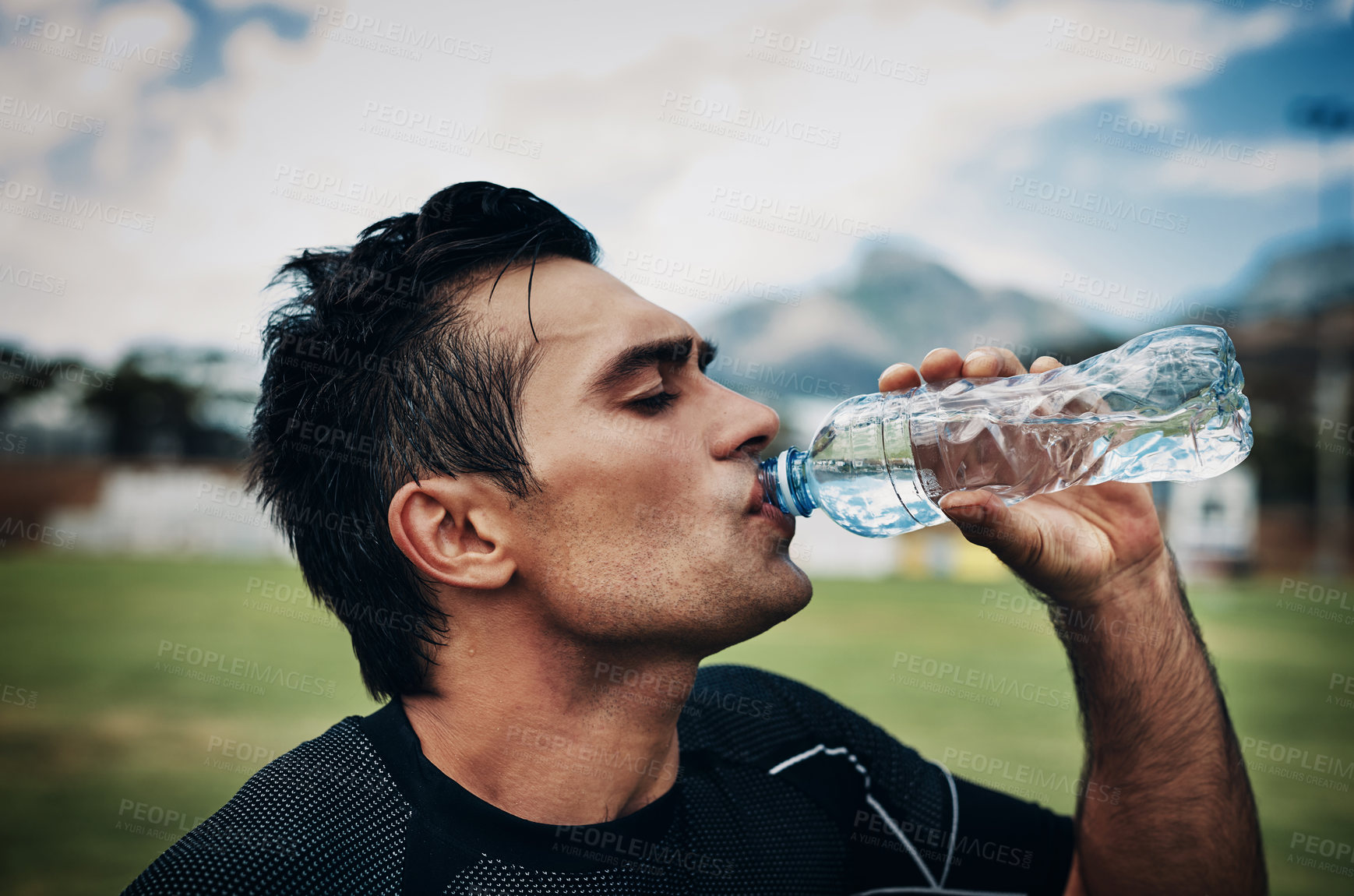 Buy stock photo Cropped shot of a handsome young rugby player drinking water while standing on the field during the day