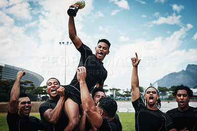 Buy stock photo Cropped shot of a handsome young rugby player holding up a trophy while celebrating with his team on the field