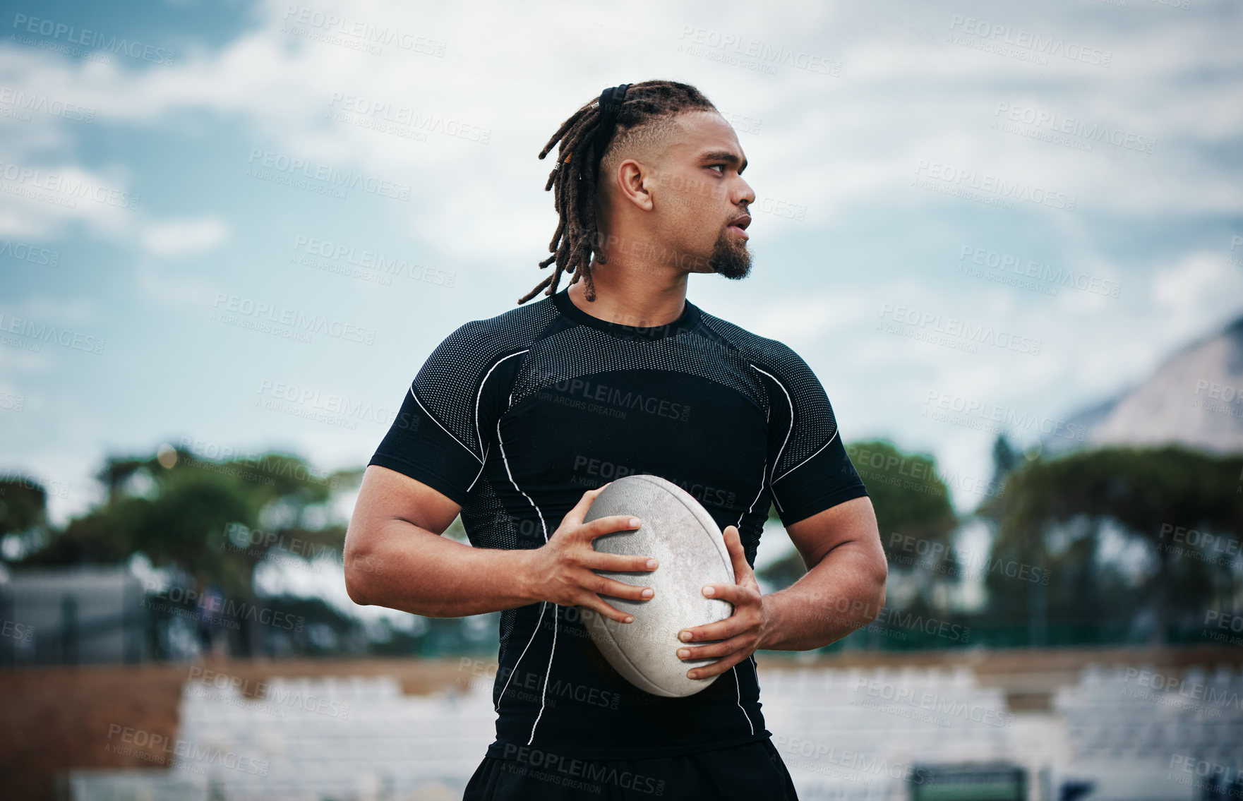 Buy stock photo Cropped shot of a handsome young rugby player holding a rugby ball while standing on the field
